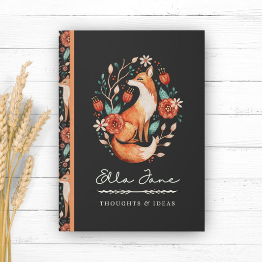 Hardcover journal with fox design on cover and fox pattern on back. Journal is personalized with the first name of recipient, and says thoughts and ideas under the name. Fox design features floral elements in a vintage illustrated style.